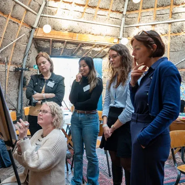 Deelnemers aan de workshop kijken geconcentreerd naar een flipover