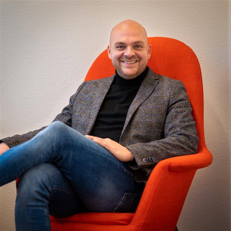 portretfoto van dennis bruins die op een oranje stoel zit